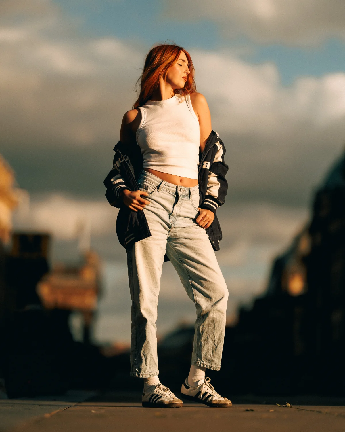 Full-body fashion shot of a woman with red hair in a white crop top and light-wash jeans during golden hour.