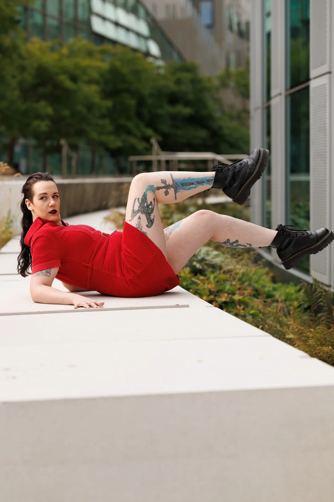 Woman in a red dress and black boots posing on a white concrete ledge outdoors.