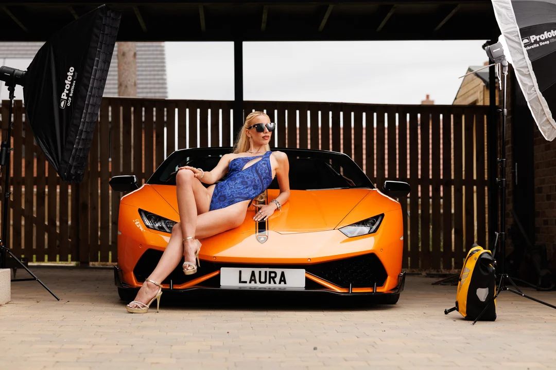 Woman in a blue swimsuit posing on an orange Lamborghini with studio lighting.