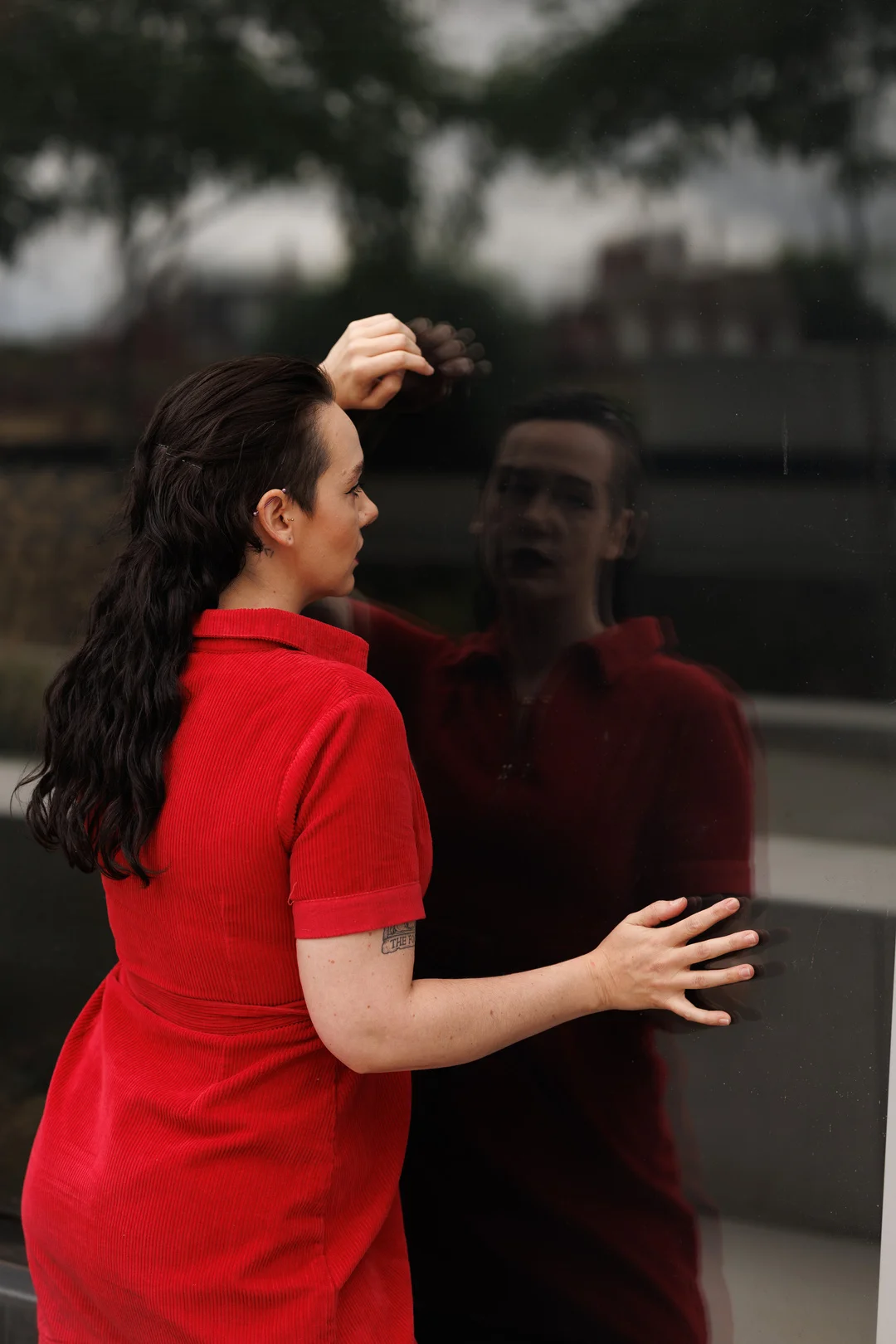 A person in a red corduroy dress posing against a dark reflective surface, creating a mirrored image.