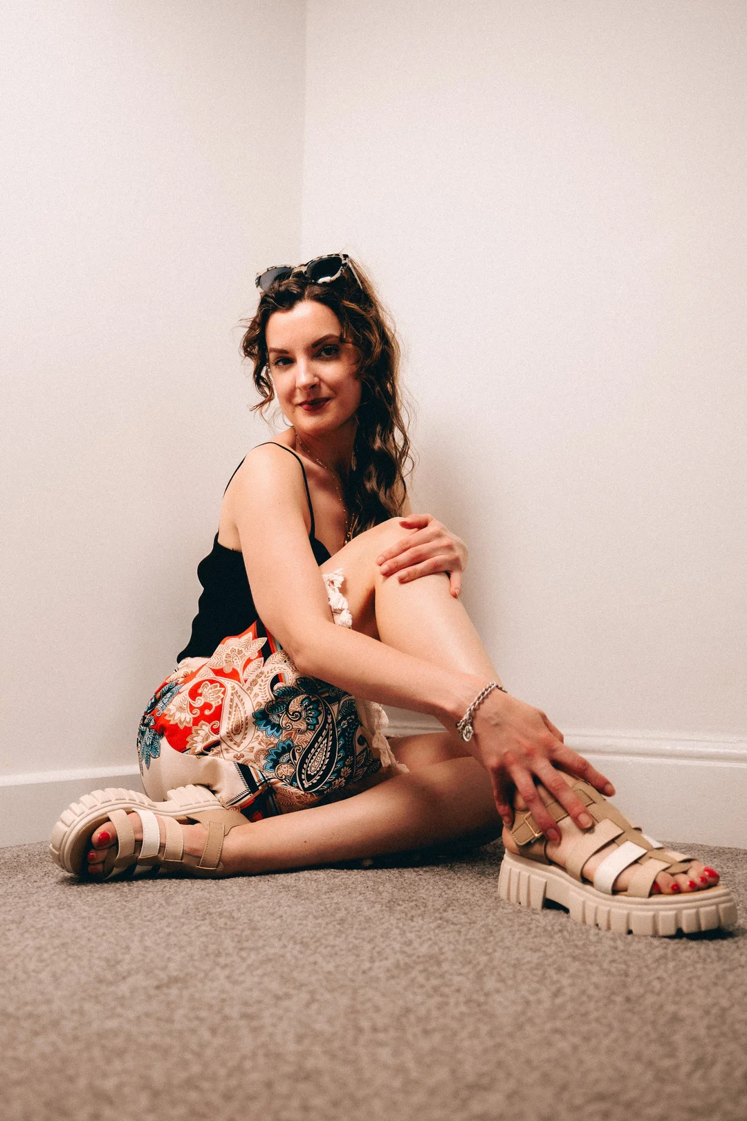 A woman in a black top and colorful paisley skirt sitting on a carpeted floor, posing for a portrait.