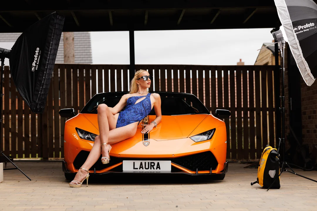 Woman in a blue swimsuit posing on an orange Lamborghini with studio lighting.