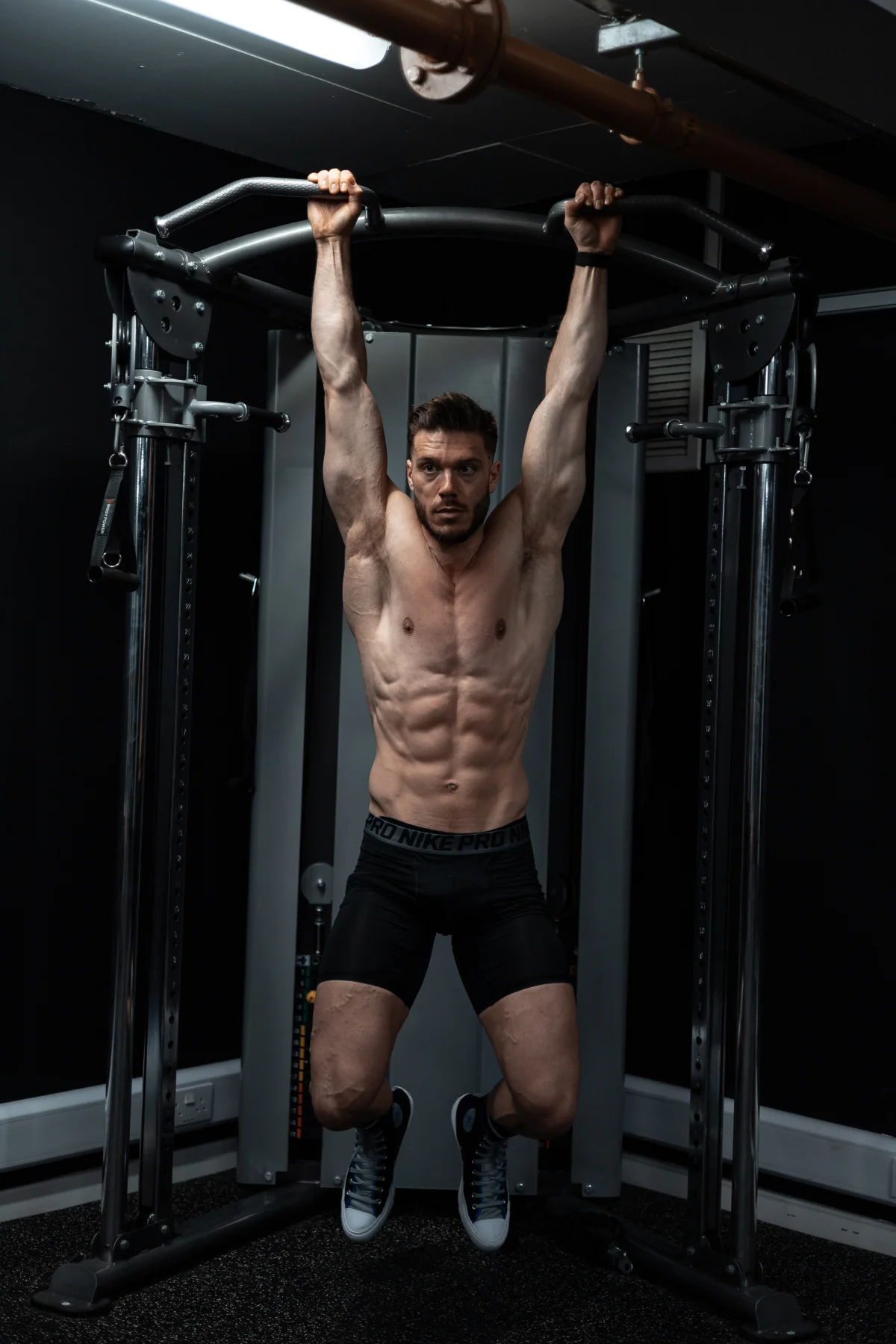 Muscular man performing a pull-up in a gym, wearing black compression shorts.