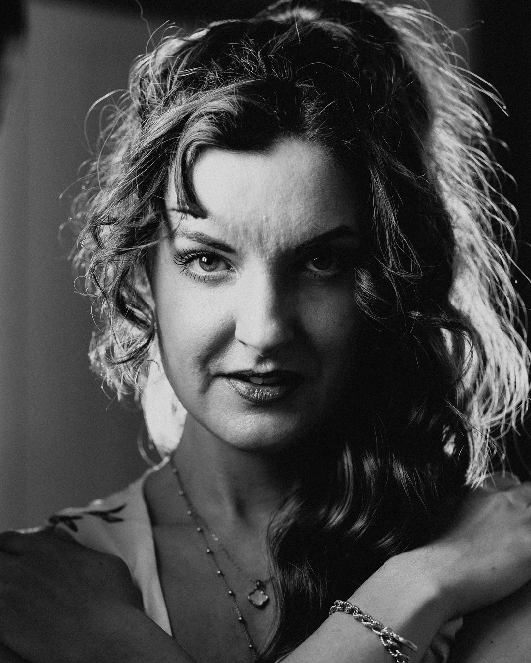 Black and white close-up portrait of a woman with curly hair and a moody expression.