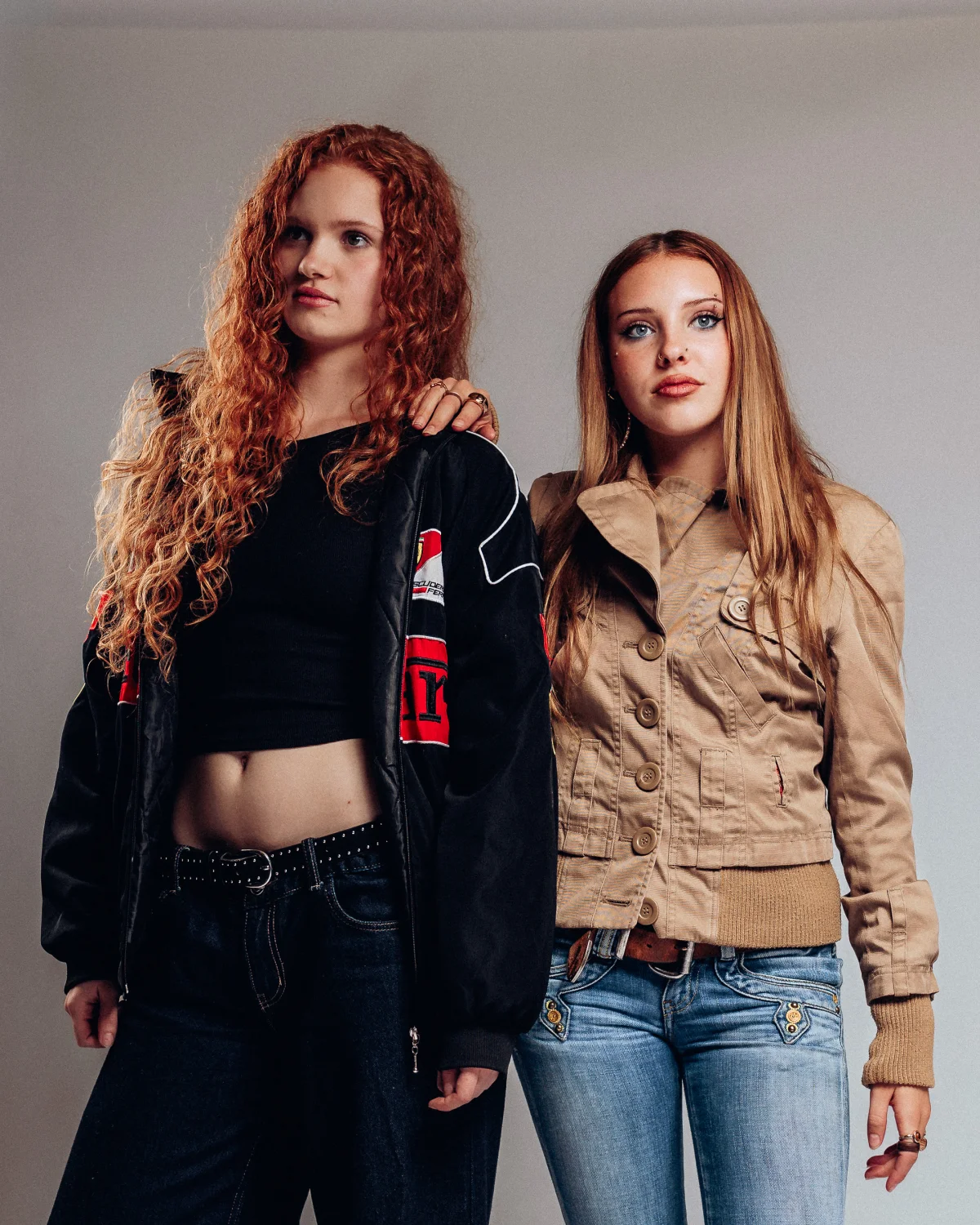 Two young women posing together against a plain grey background in stylish jackets.