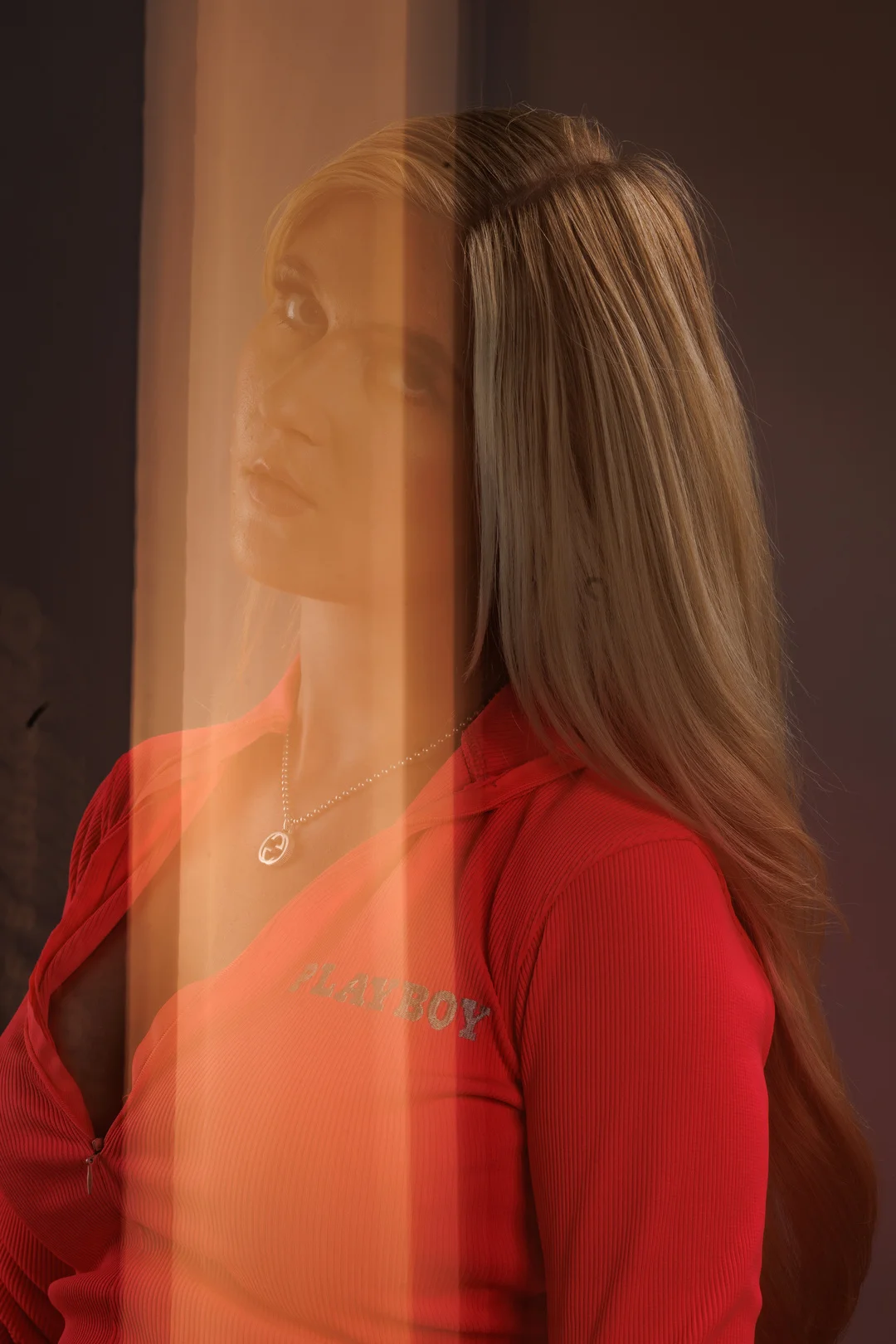 Portrait of a blonde woman in a red zip-up top with orange vertical light streaks overlaying the scene.