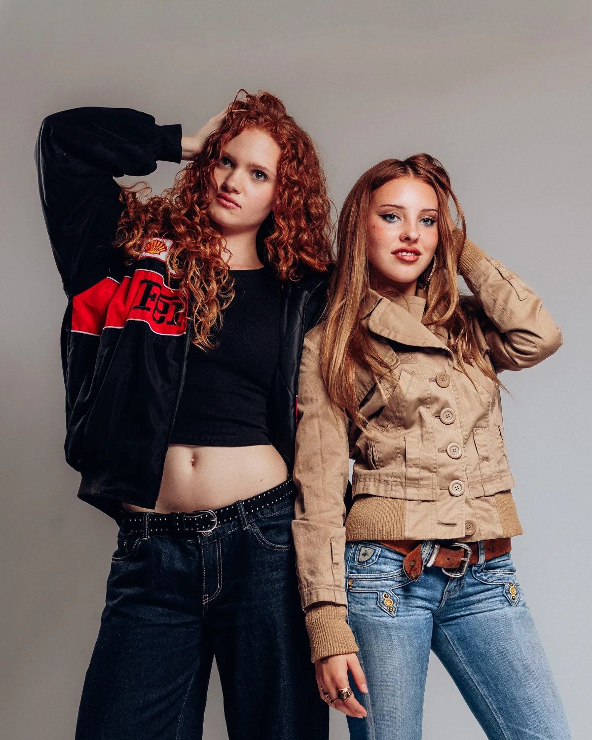 Two young women with red hair posing in a studio, wearing casual jackets and jeans.
