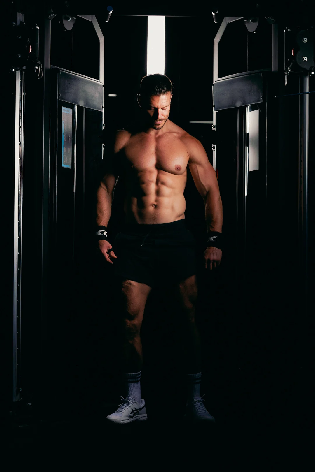 Muscular man posing in a gym with dramatic low-key lighting highlighting his physique.