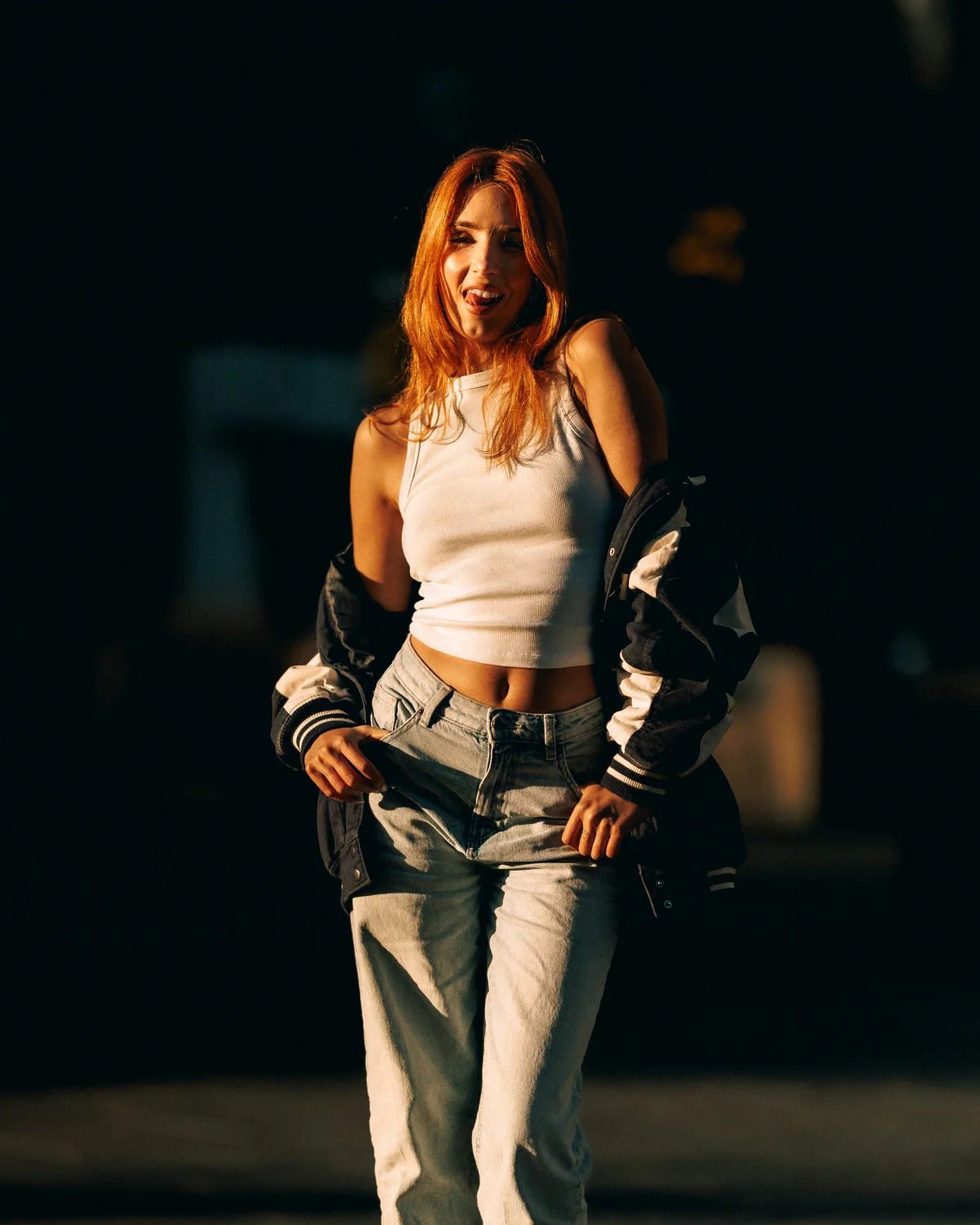 Woman with red hair in a white crop top and jeans posing in golden hour light.