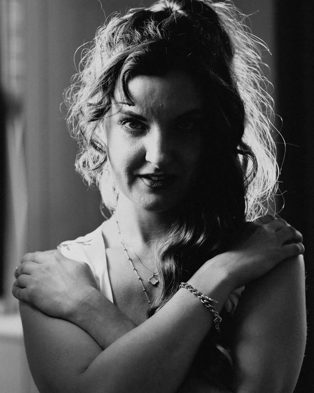 Moody black and white portrait of a woman with curly hair and crossed arms.