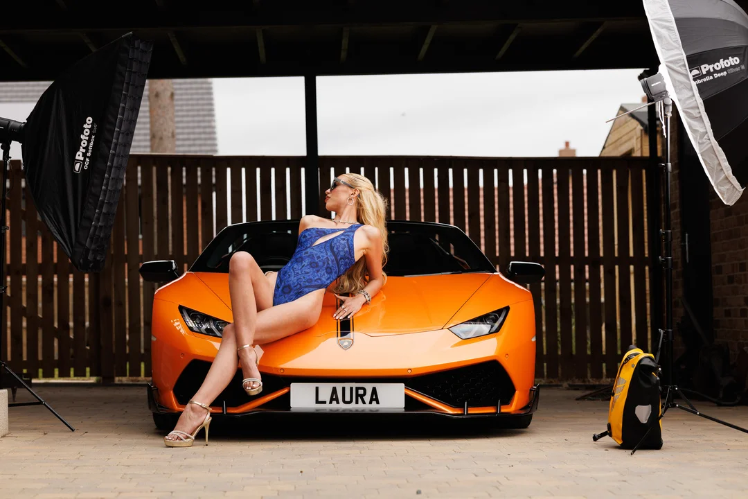 Woman in a blue swimsuit posing on an orange Lamborghini with professional studio lighting.