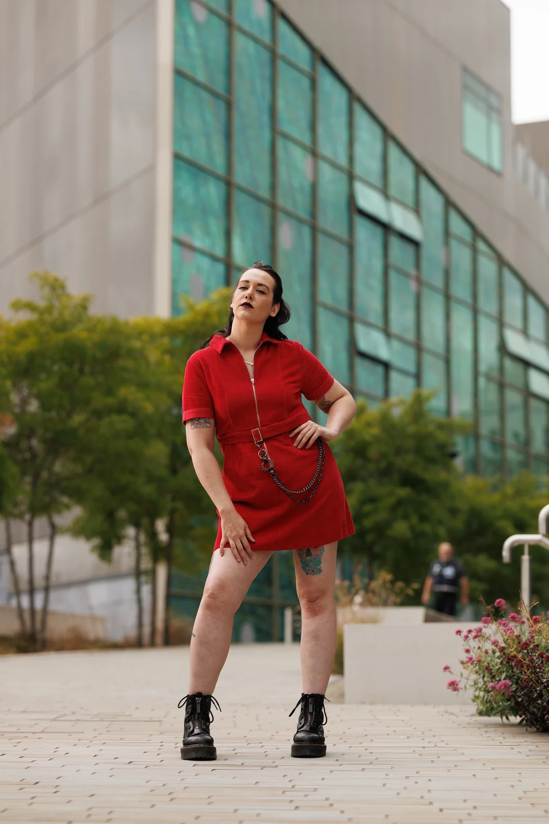 A person in a red mini dress and black boots posing confidently in front of a modern glass building.