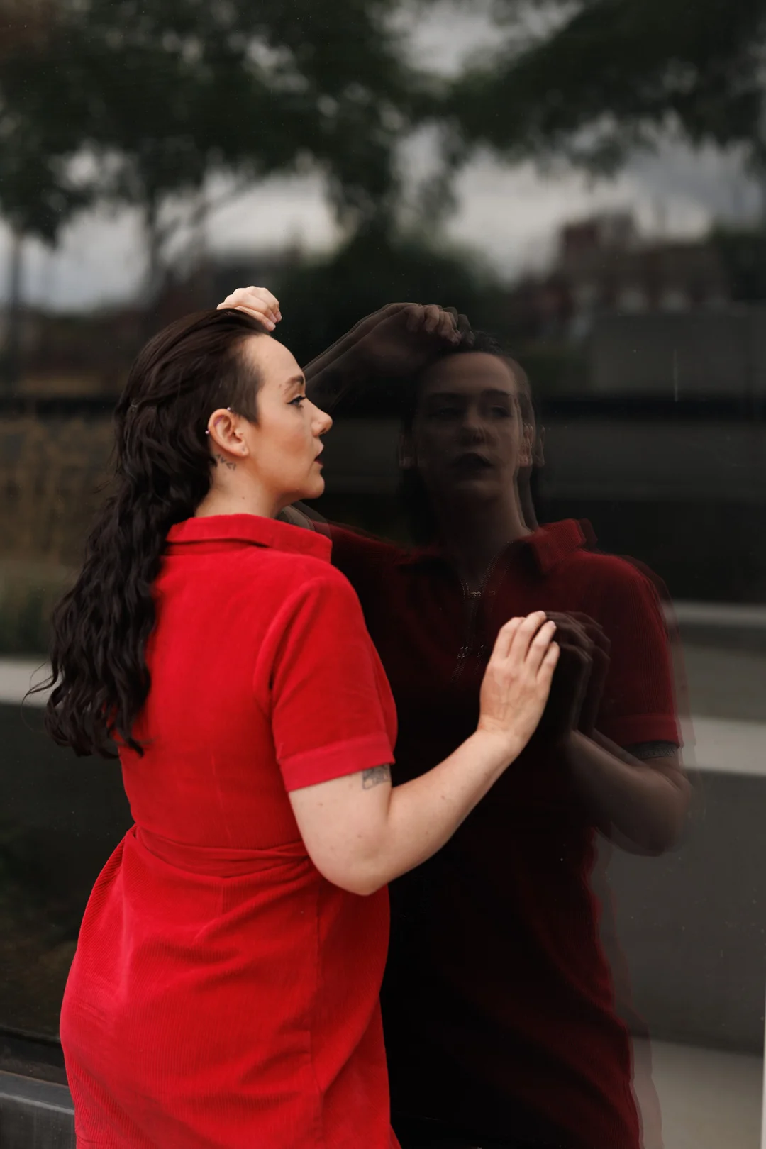 A woman in a red dress gazing at her blurred reflection in a glass window, creating a moody, artistic atmosphere.