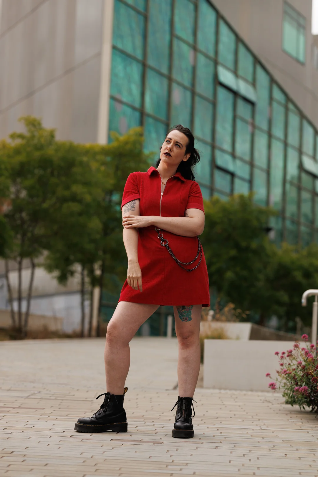 A woman in a short red dress and black boots posing in front of a modern glass building.