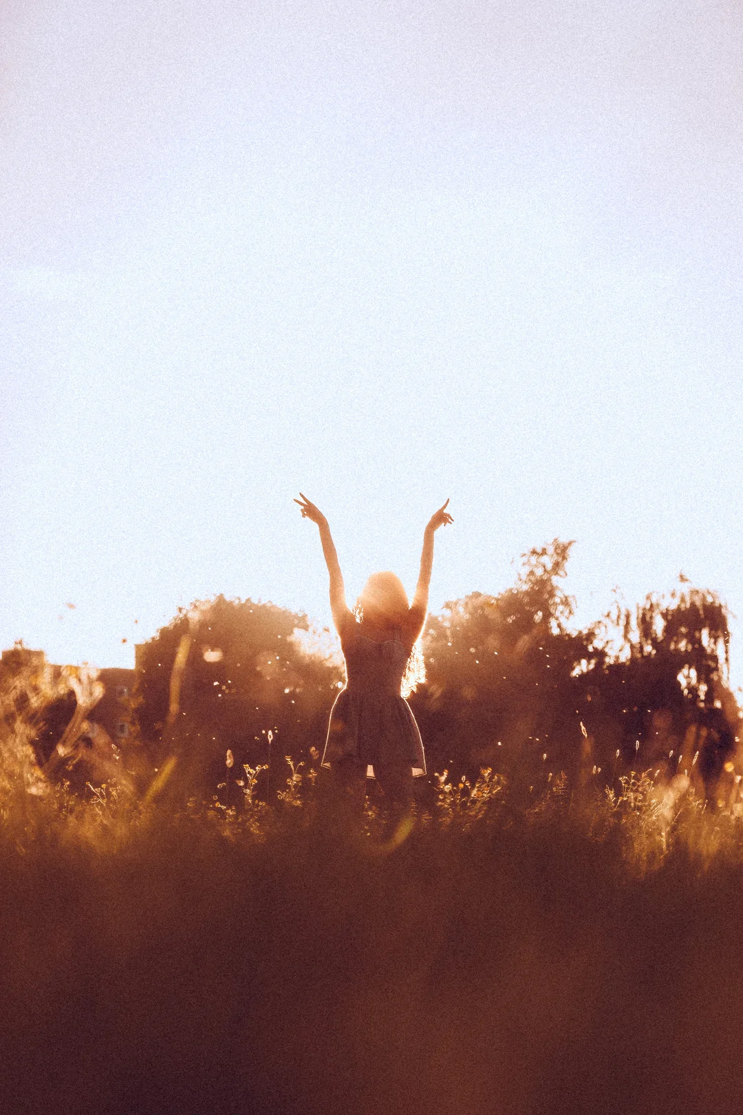 Silhouette of a woman with arms raised in a golden field at sunset, conveying joy and freedom.