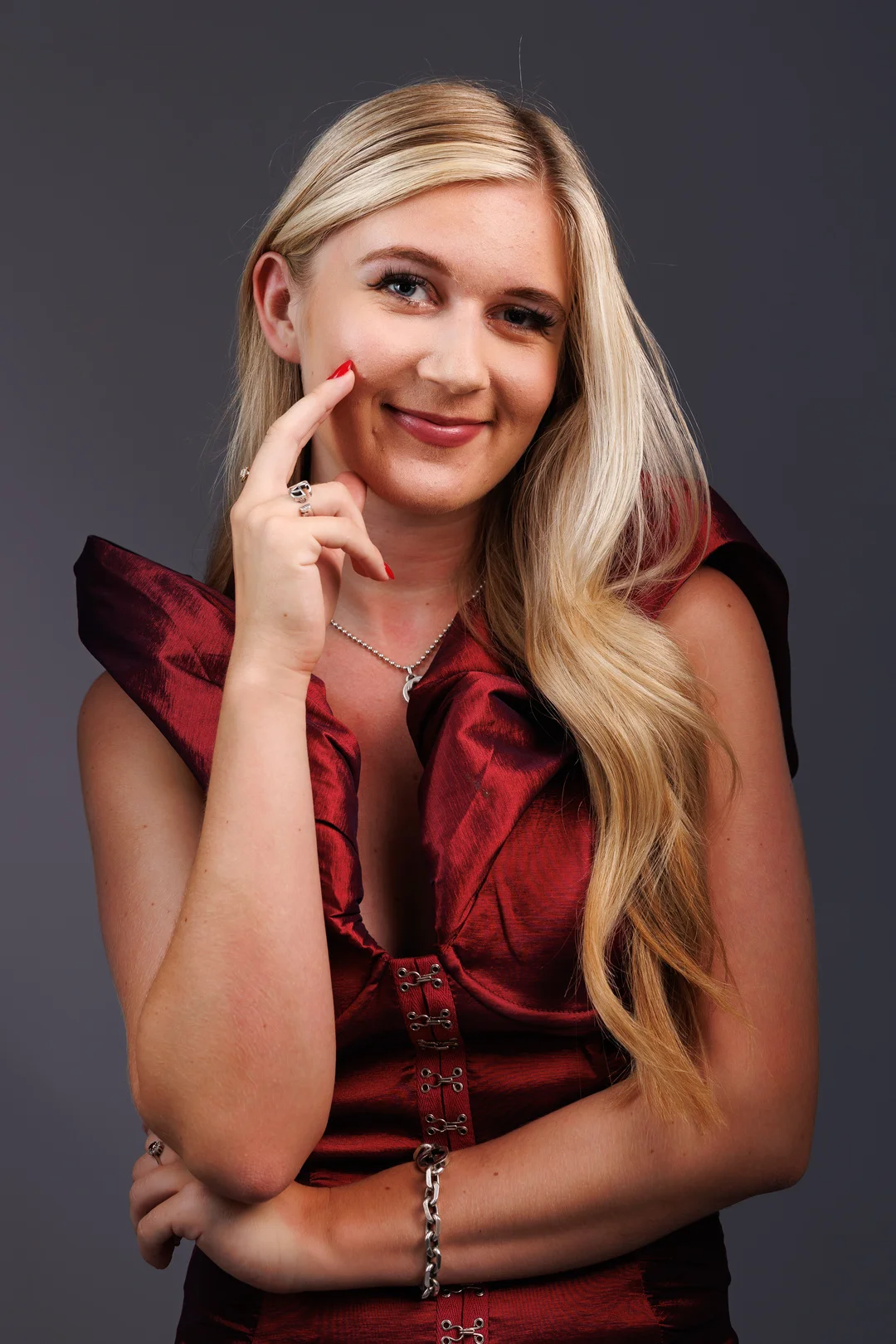 Portrait of a blonde woman in a red dress posing against a grey studio background.