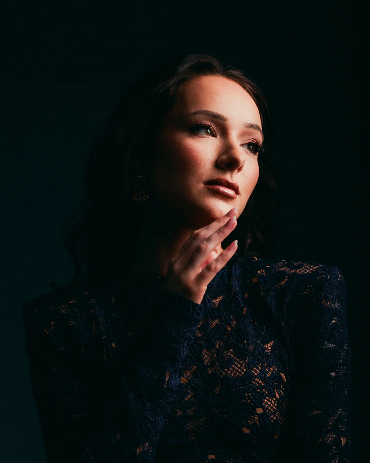 Moody close-up portrait of a woman in a dark lace dress looking thoughtfully to the side.