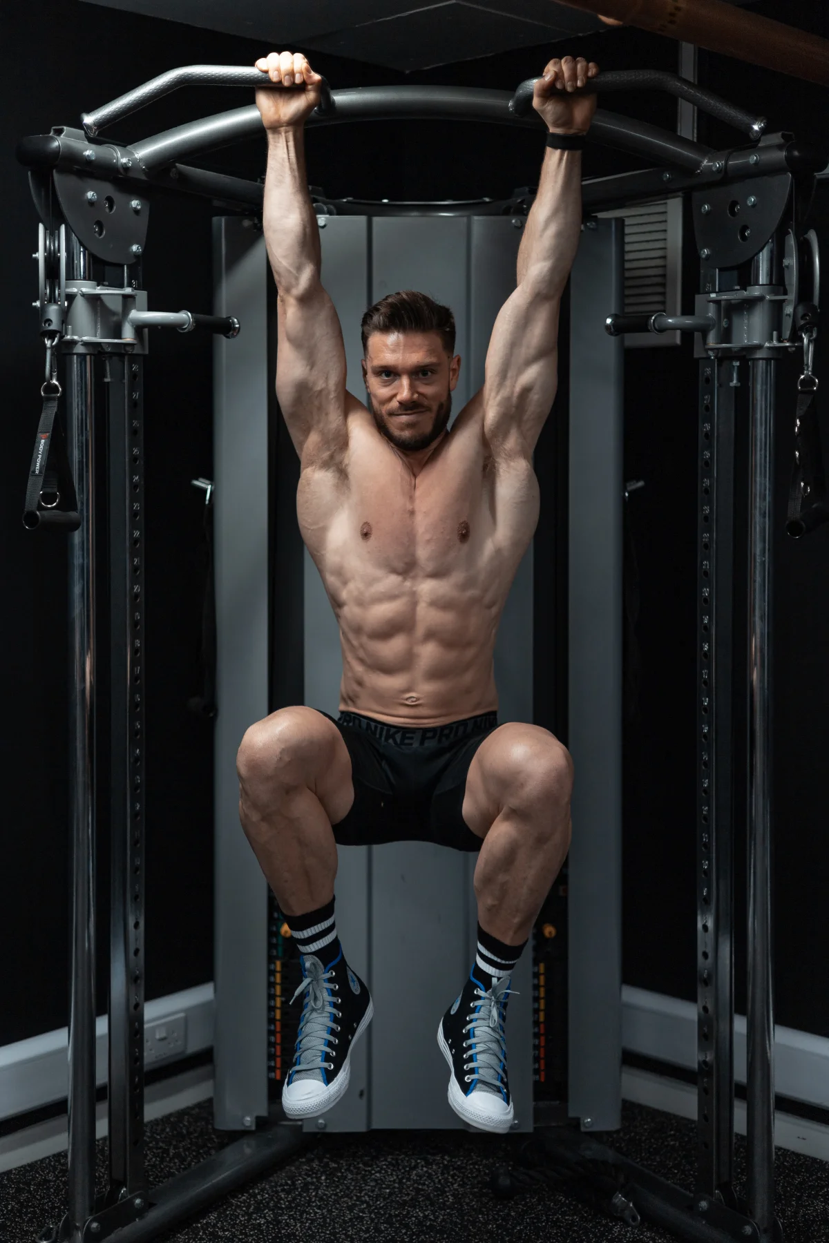 Muscular man hanging from a pull-up bar in a gym, showcasing his physique.