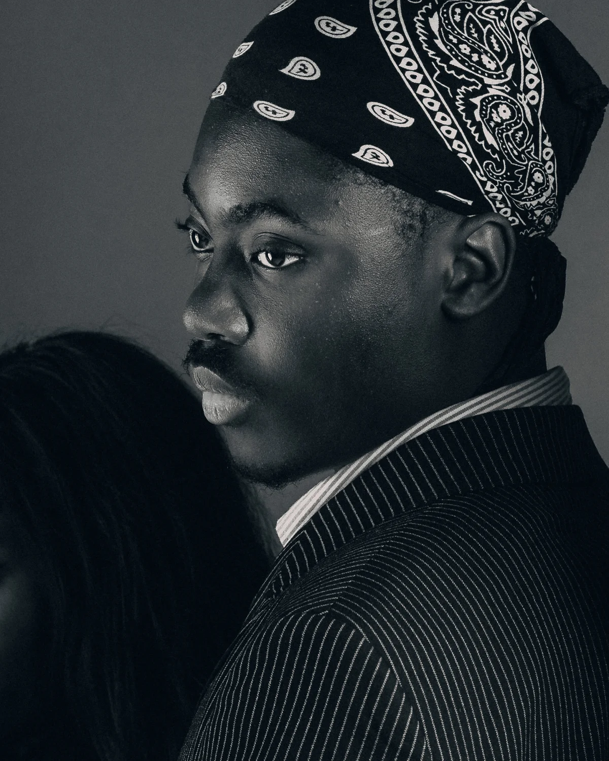 Black and white close-up portrait of a man in a bandana and pinstripe suit, looking thoughtfully to the side.