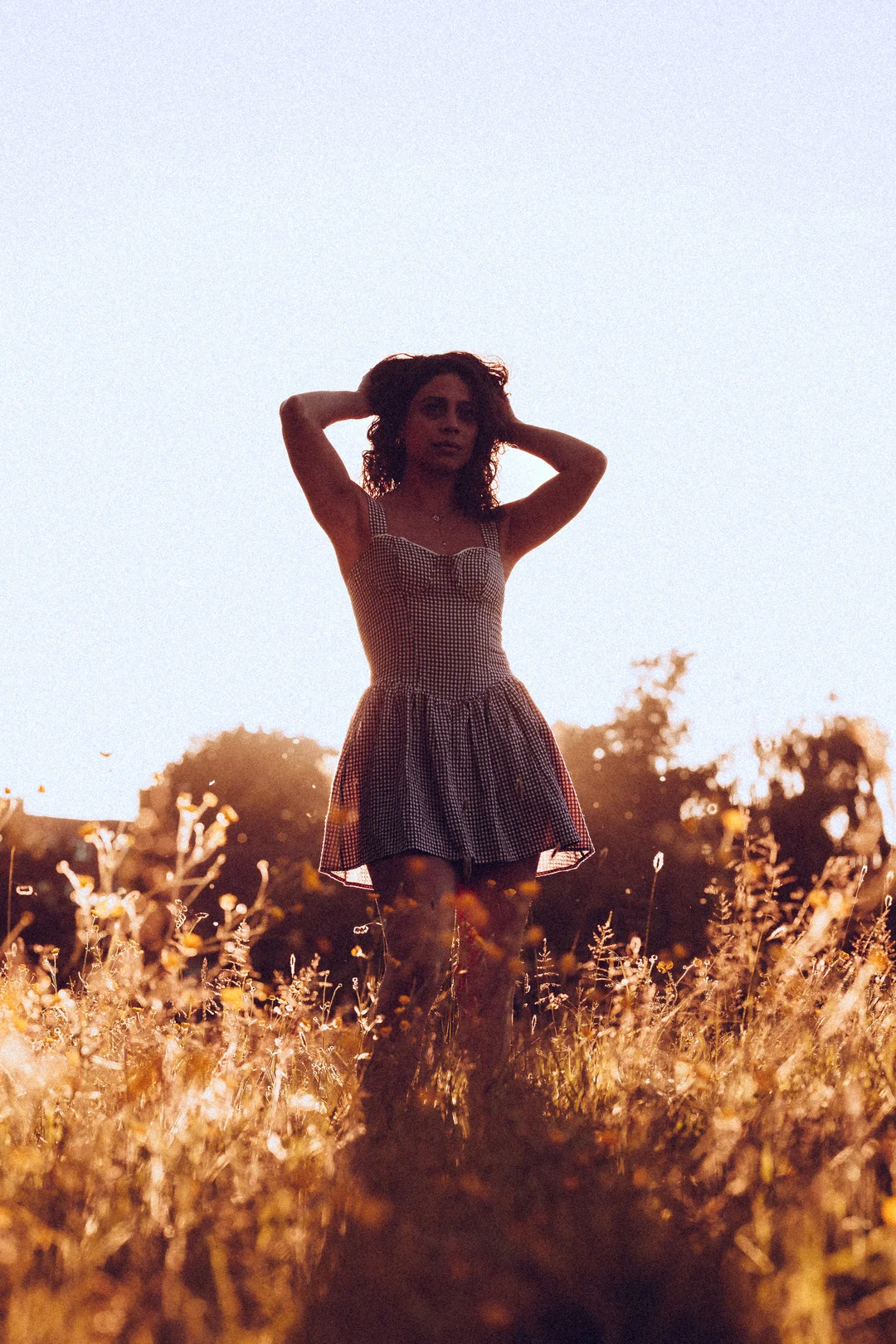 Woman in a red and white checkered dress posing in a golden field during sunset.