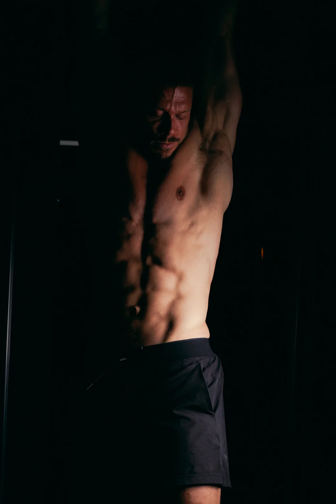 Low-key portrait of a shirtless man, emphasizing muscle definition with dramatic lighting.