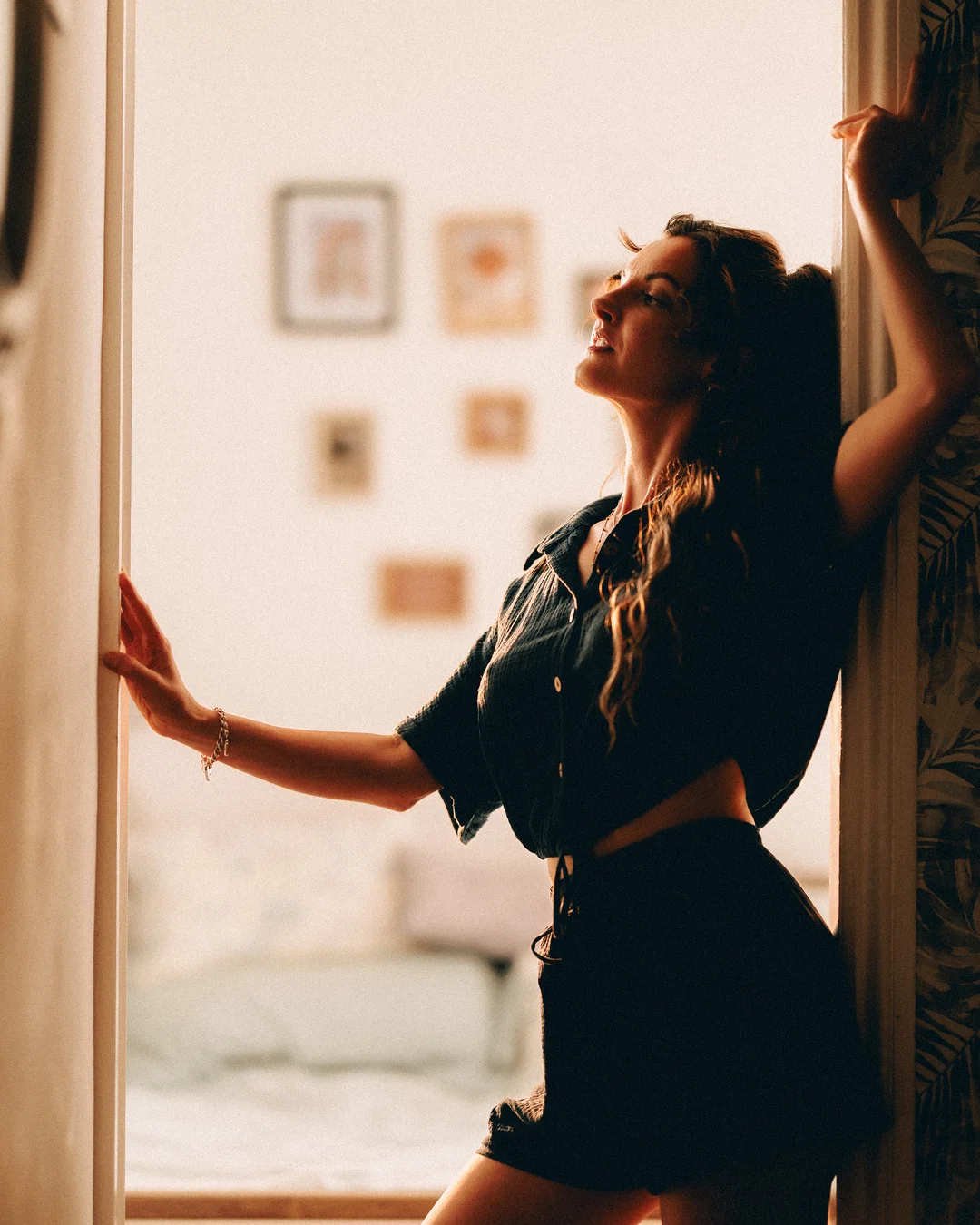 A woman in a black outfit posing in a doorway with warm, moody lighting.
