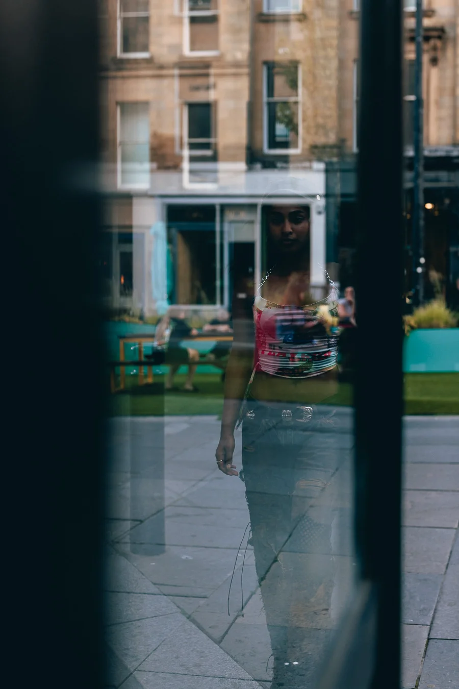 A moody portrait of a person reflected in a glass window with an urban building in the background.