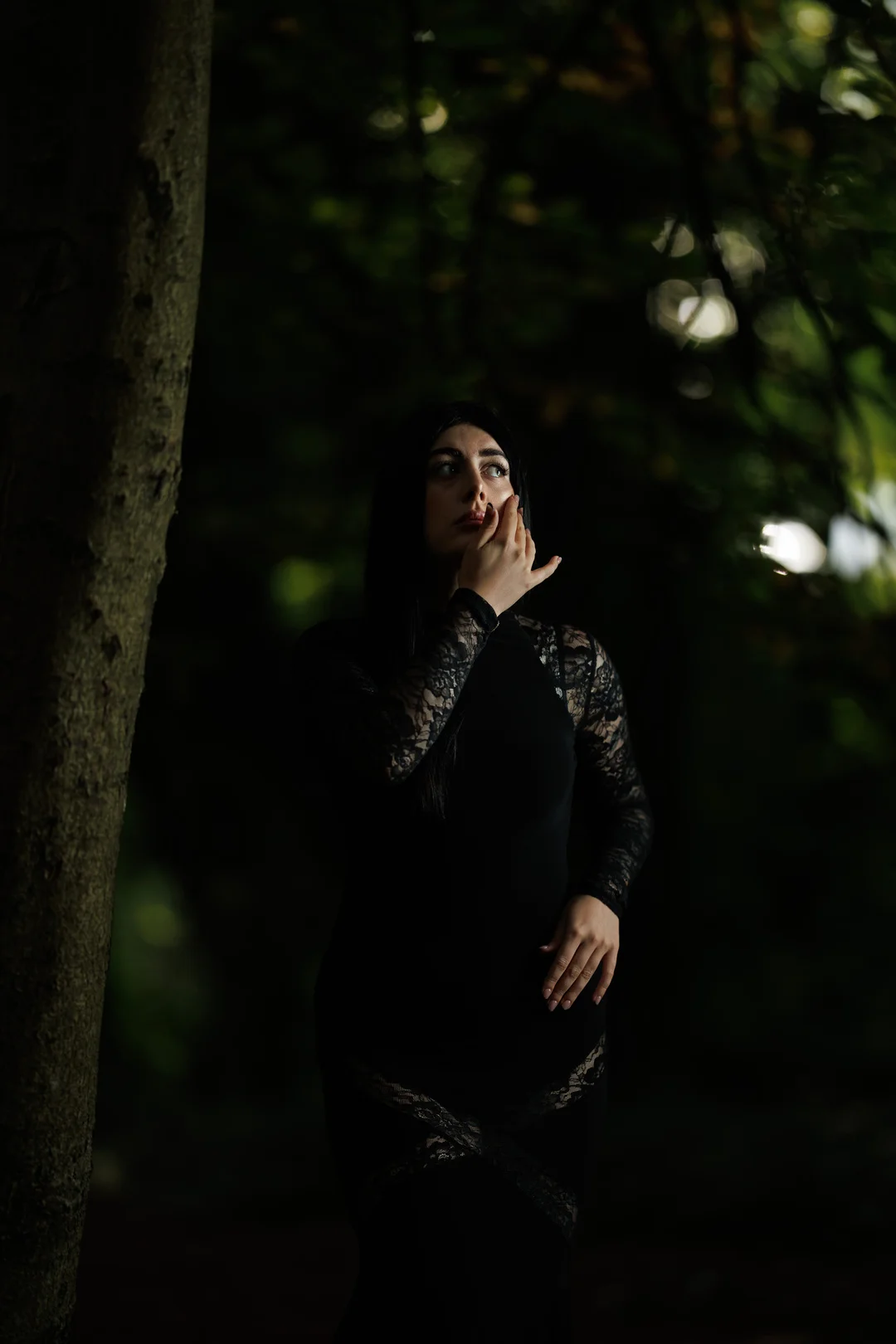 Woman in a black lace dress posing in a dark, moody forest.
