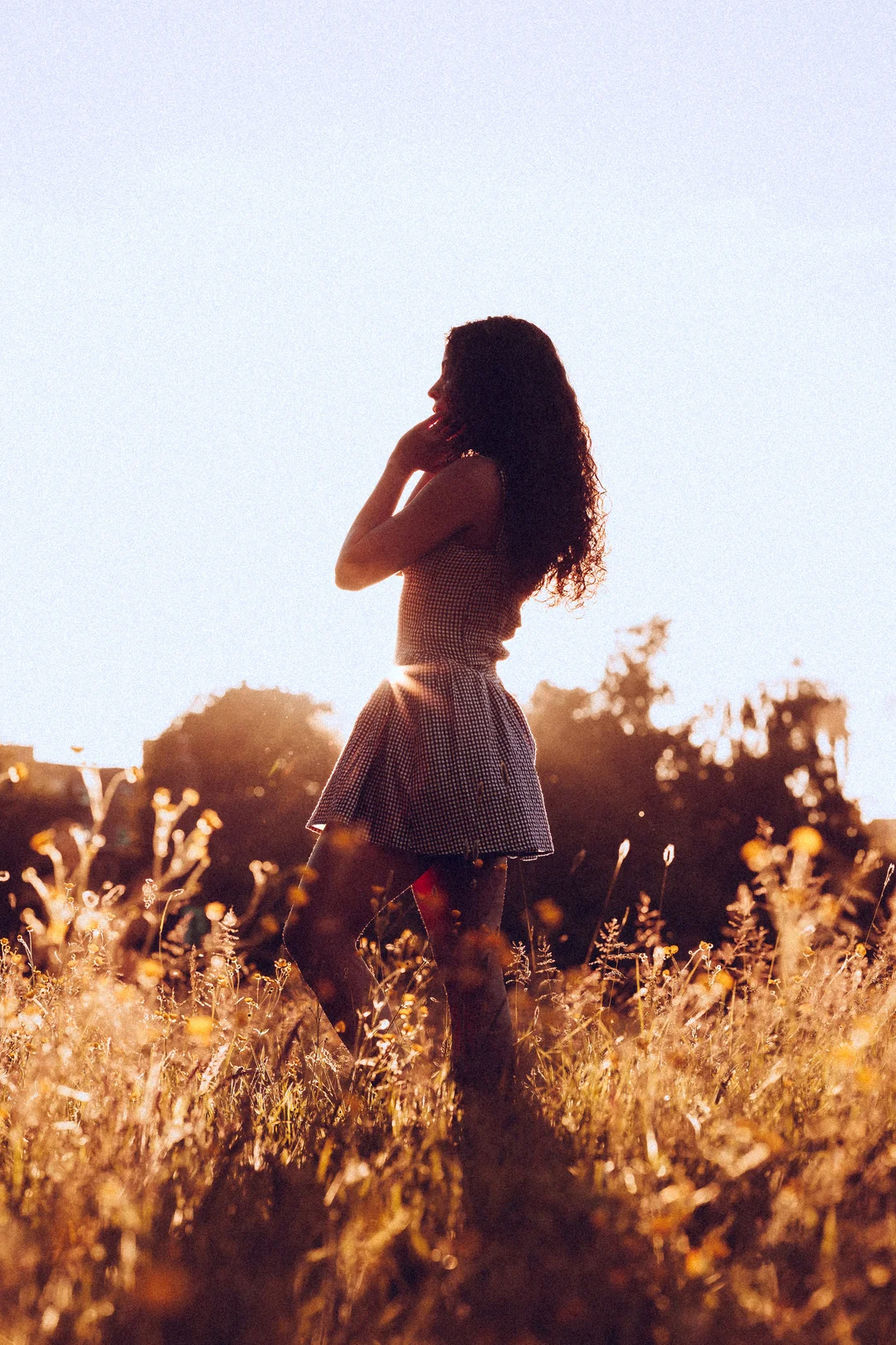 Silhouette of a woman in a short dress standing in a golden field during sunset.