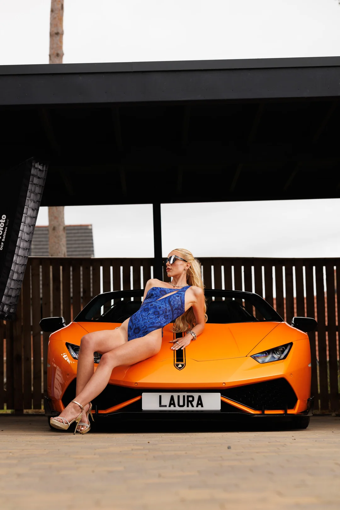 Woman in a blue swimsuit posing on the hood of an orange luxury sports car.