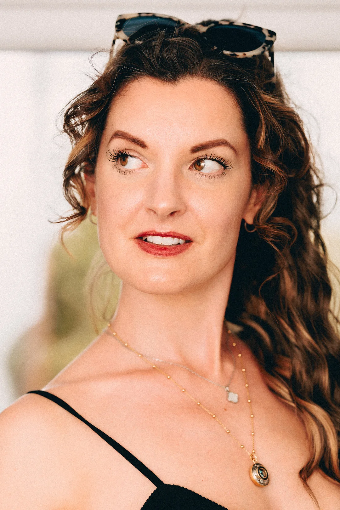 Close-up portrait of a woman with curly brown hair and sunglasses on her head, looking off-camera.