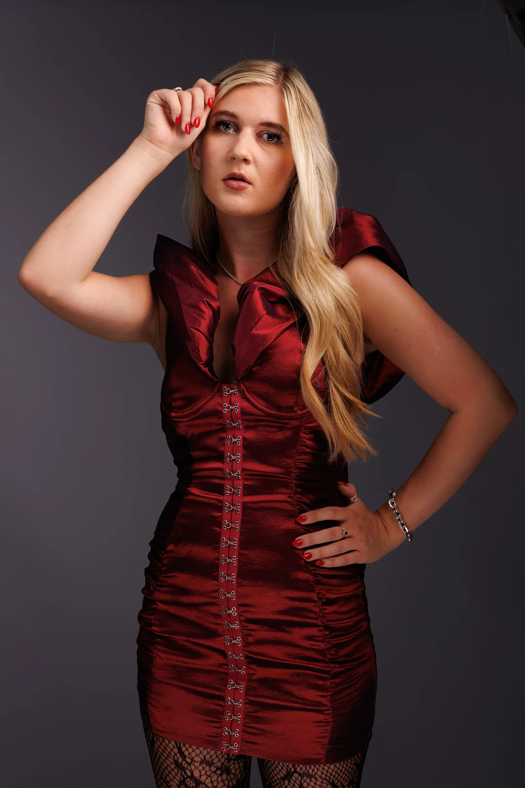Blonde woman in a red satin dress posing against a dark grey studio background.