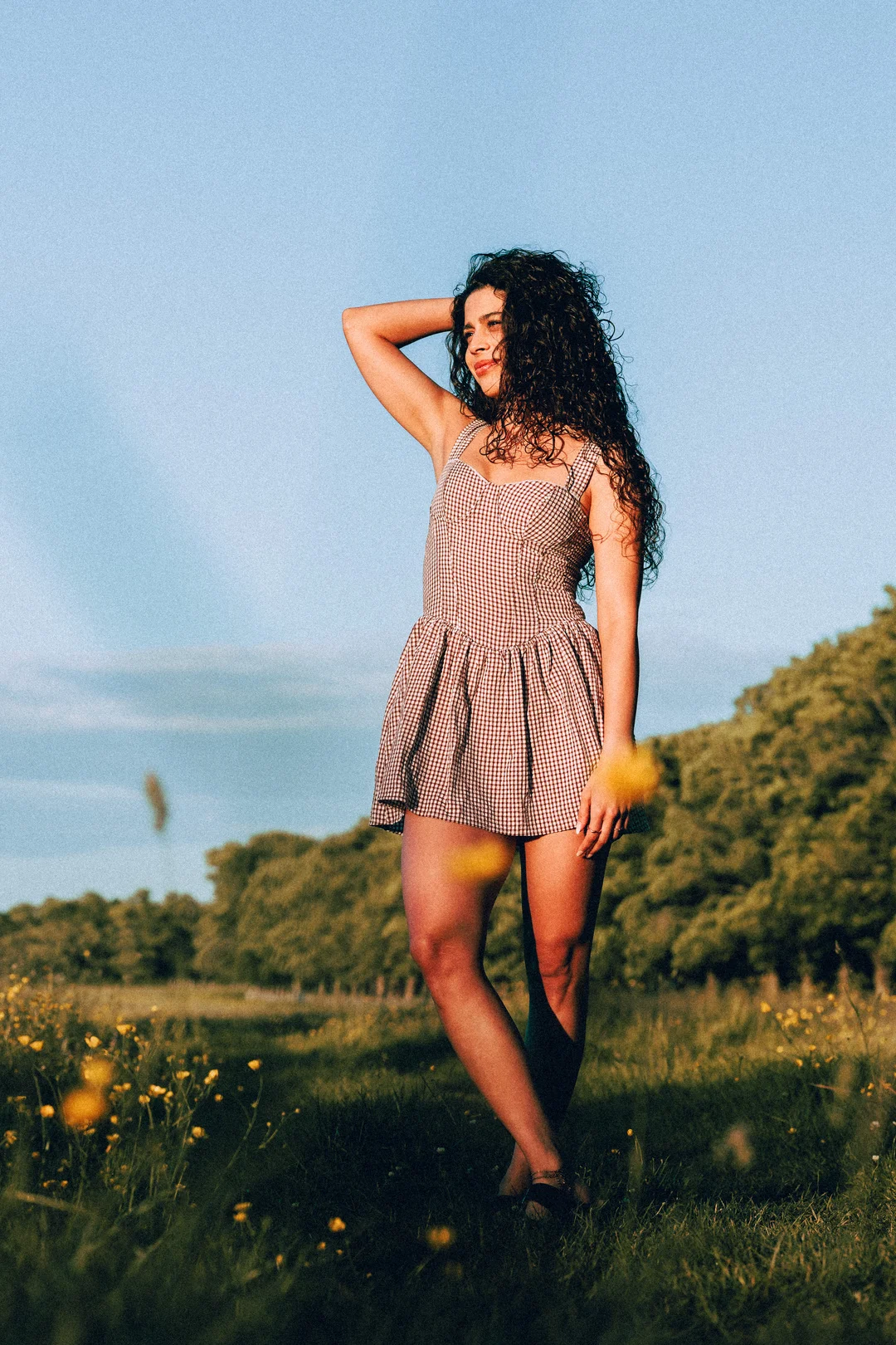 Woman with curly hair in a red gingham dress posing in a sunny meadow