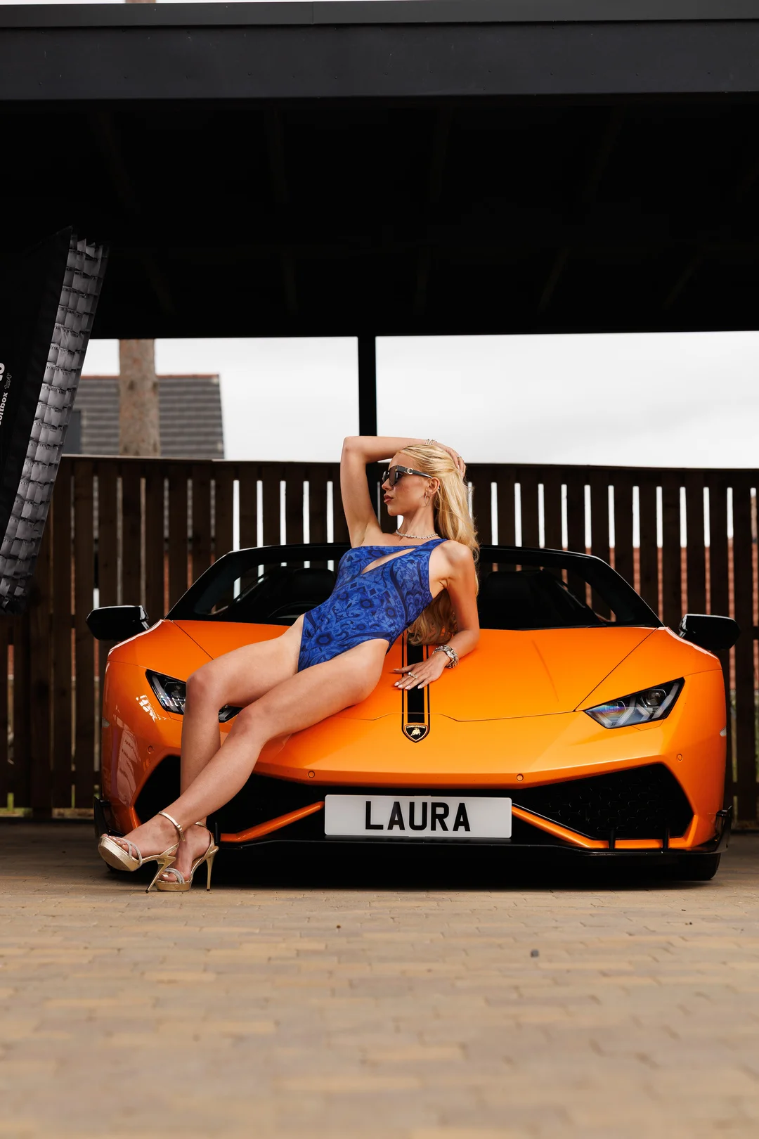 Woman in a blue swimsuit posing on the hood of an orange luxury sports car.