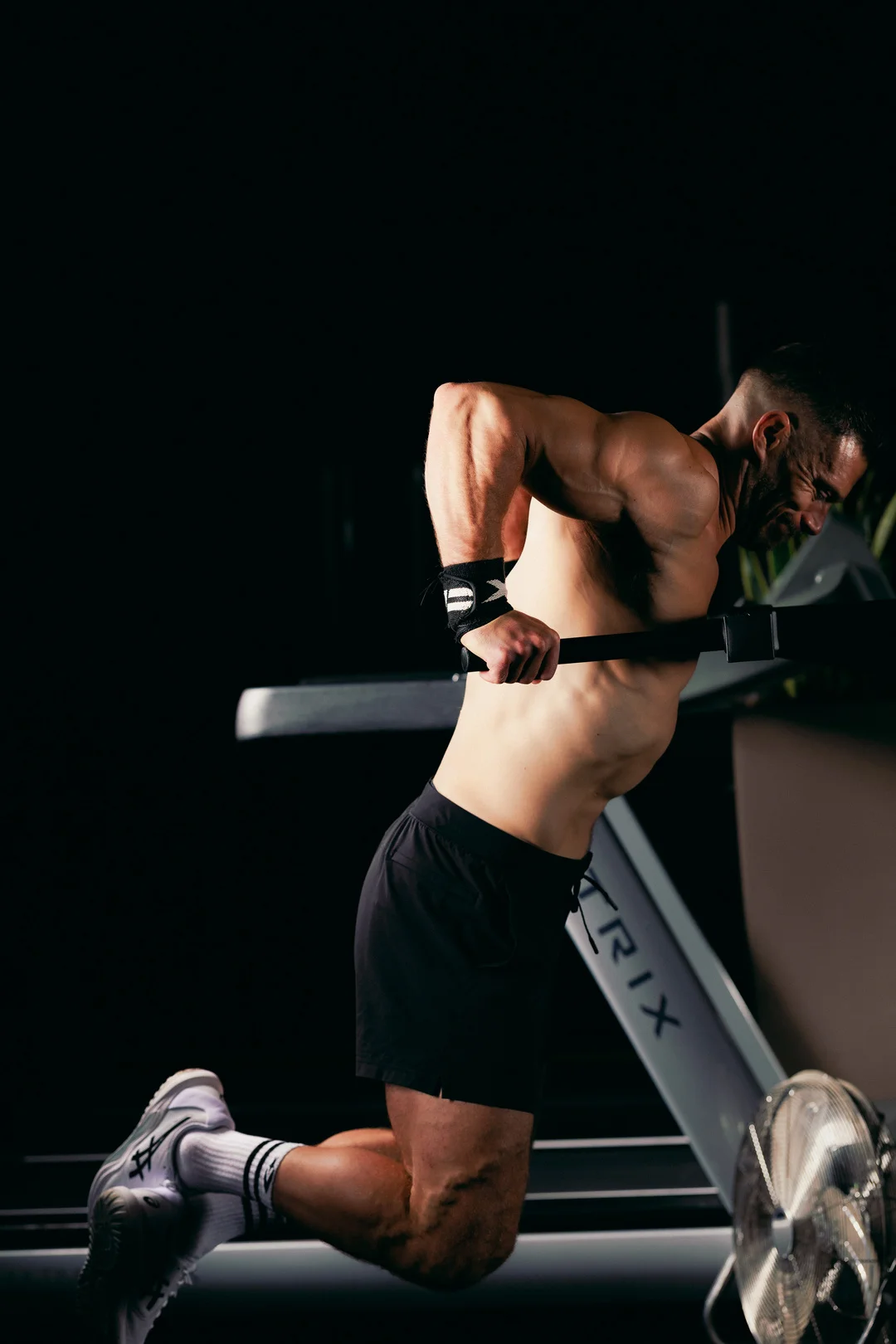 Muscular man performing a rowing exercise on a gym machine against a dark background.