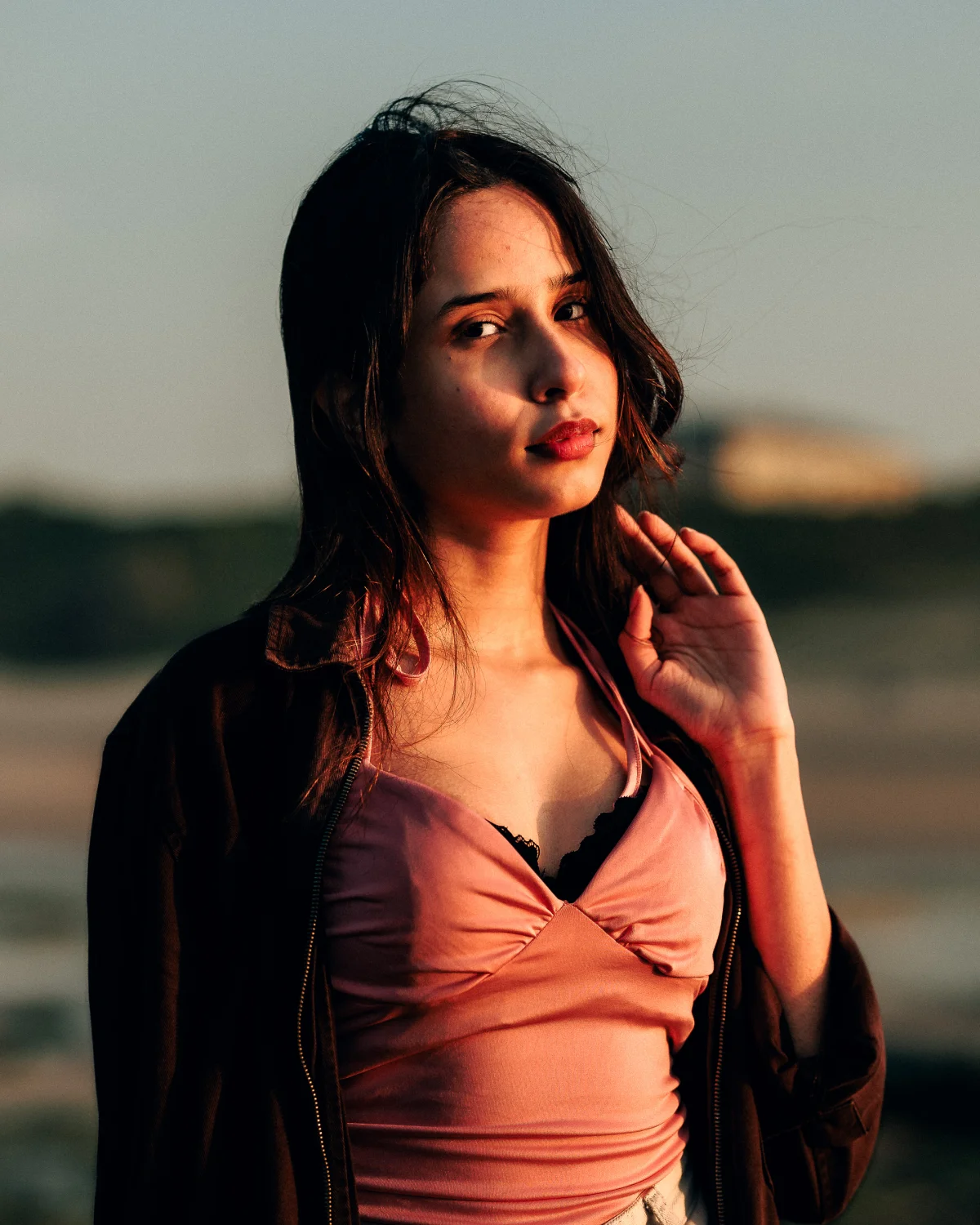 Portrait of a young woman in a pink lace top and dark jacket during golden hour outdoors.