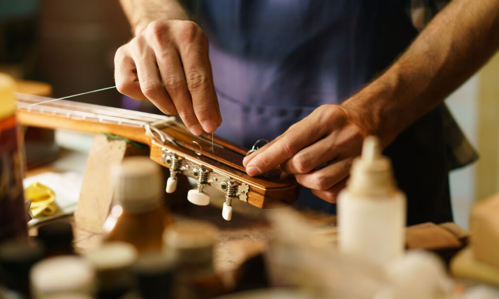 Lute maker shop and classic music instruments: young adult artisan fixing old classic guitar adding a cord and tuning the instrument. Close up of hands and palette