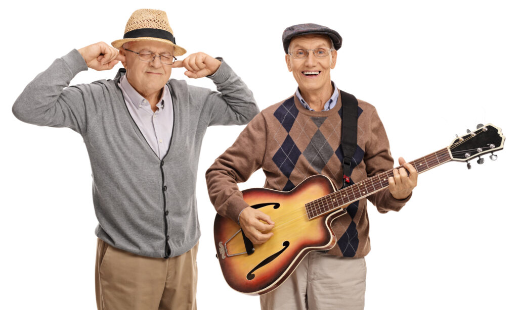 Mature man playing a guitar with another man plugging his ears with his fingers isolated on white background