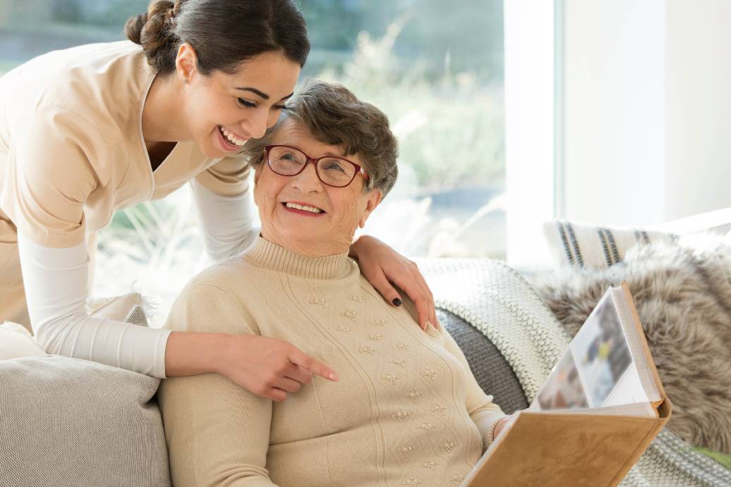 healthcare worker smiling with a memory care resident looking at a photo album