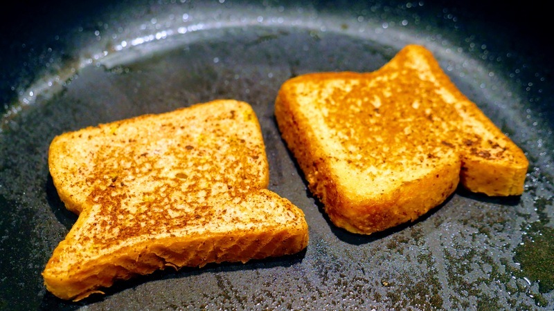 Two slices of French Toast cooking on a frying pan.