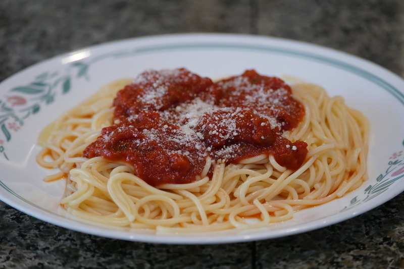 Picture of spaghetti noodles covered in sauce on a plate.