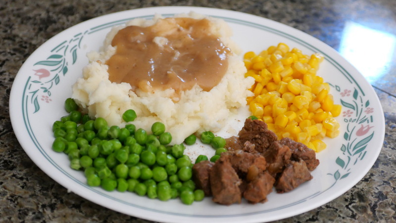 Meat, peas, corn and mashed potatoes covered in gravy on a plate.