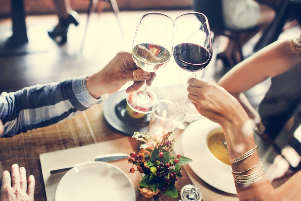 Camera focused on wine glasses as two people toast a white and a red wine