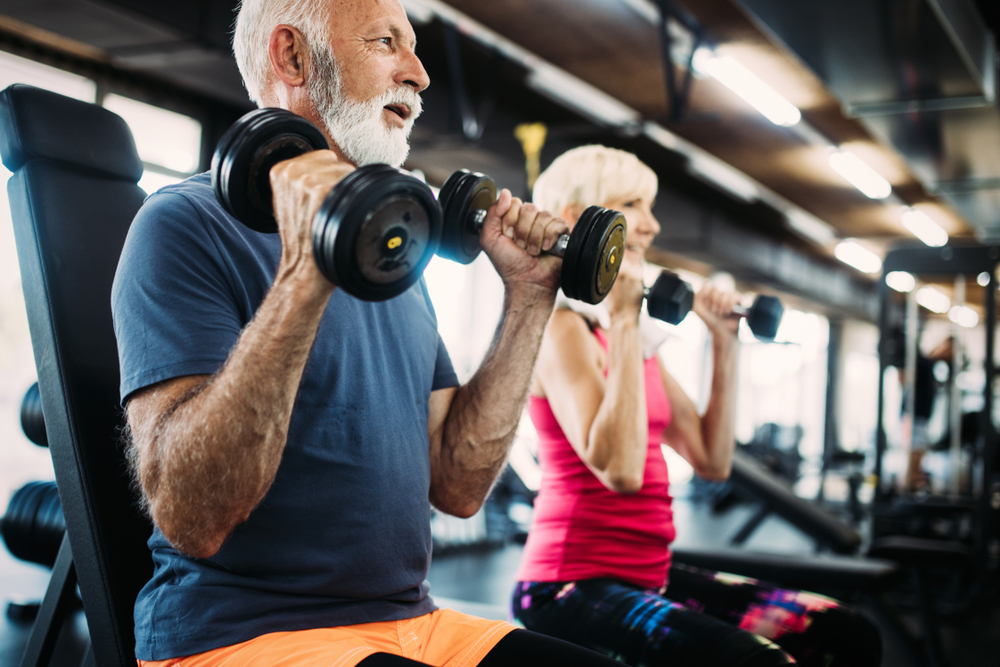 A senior man and a senior woman lift weights at the gym