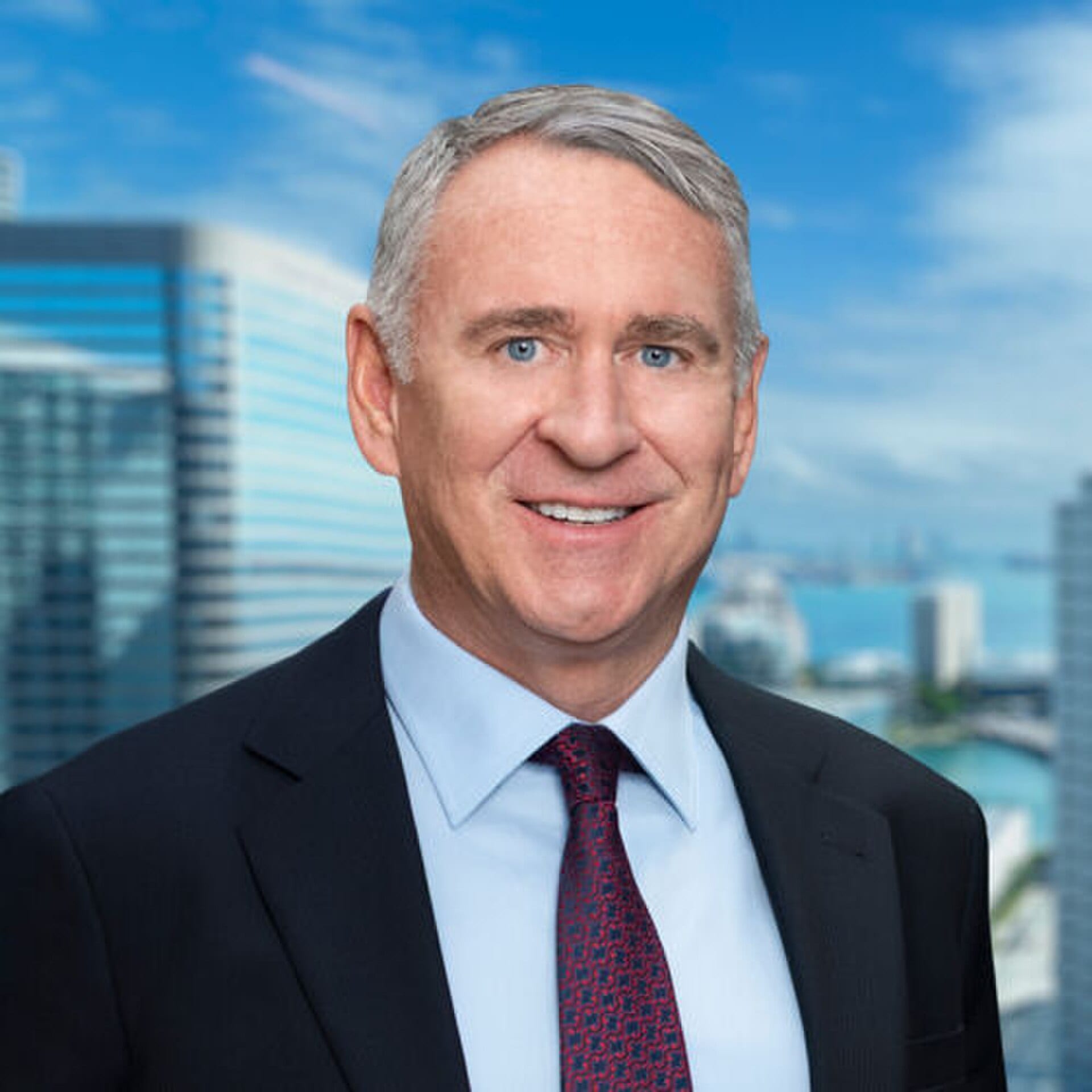 Kenneth C. Griffin in a dark suit and red patterned tie in front of a blurred Miami skyline