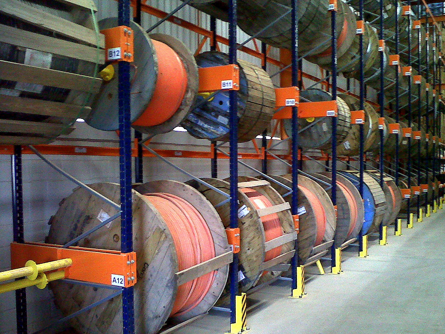 Rows of large wooden drums wound with orange fiber-optic cable stored on warehouse racking