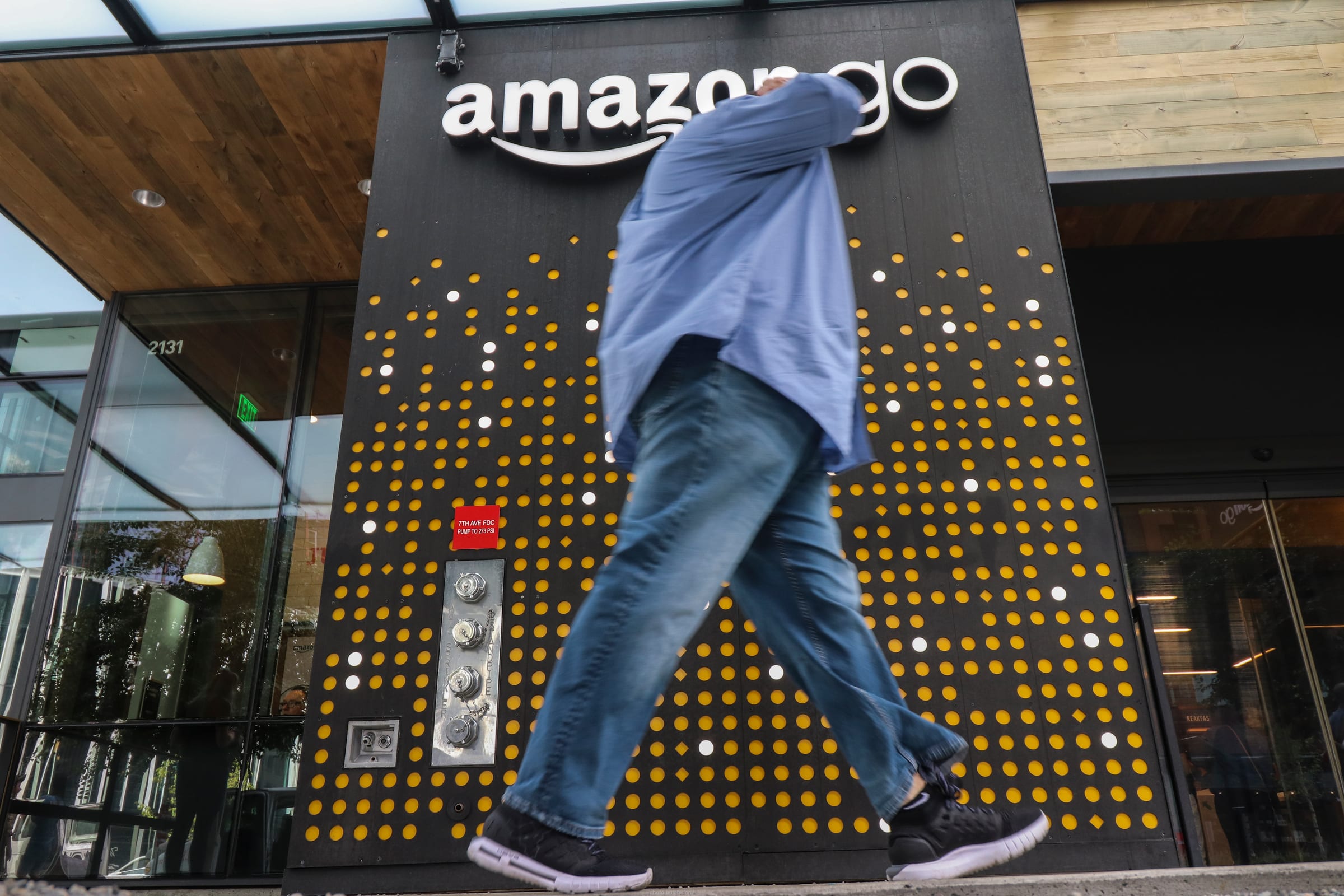 A shopper walks past the entrance of an Amazon Go store beneath the amazon go sign.