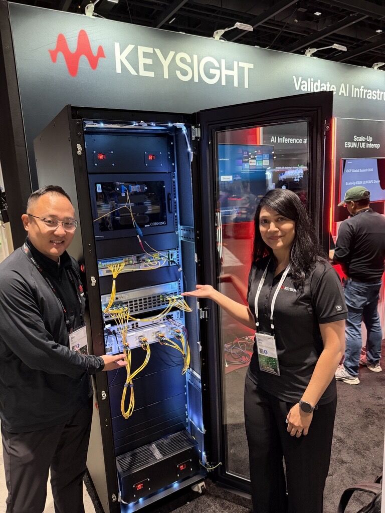 Two Keysight staff beside an open rack of network test equipment with yellow optical cables at the company's OCP Global Summit 2026 booth.