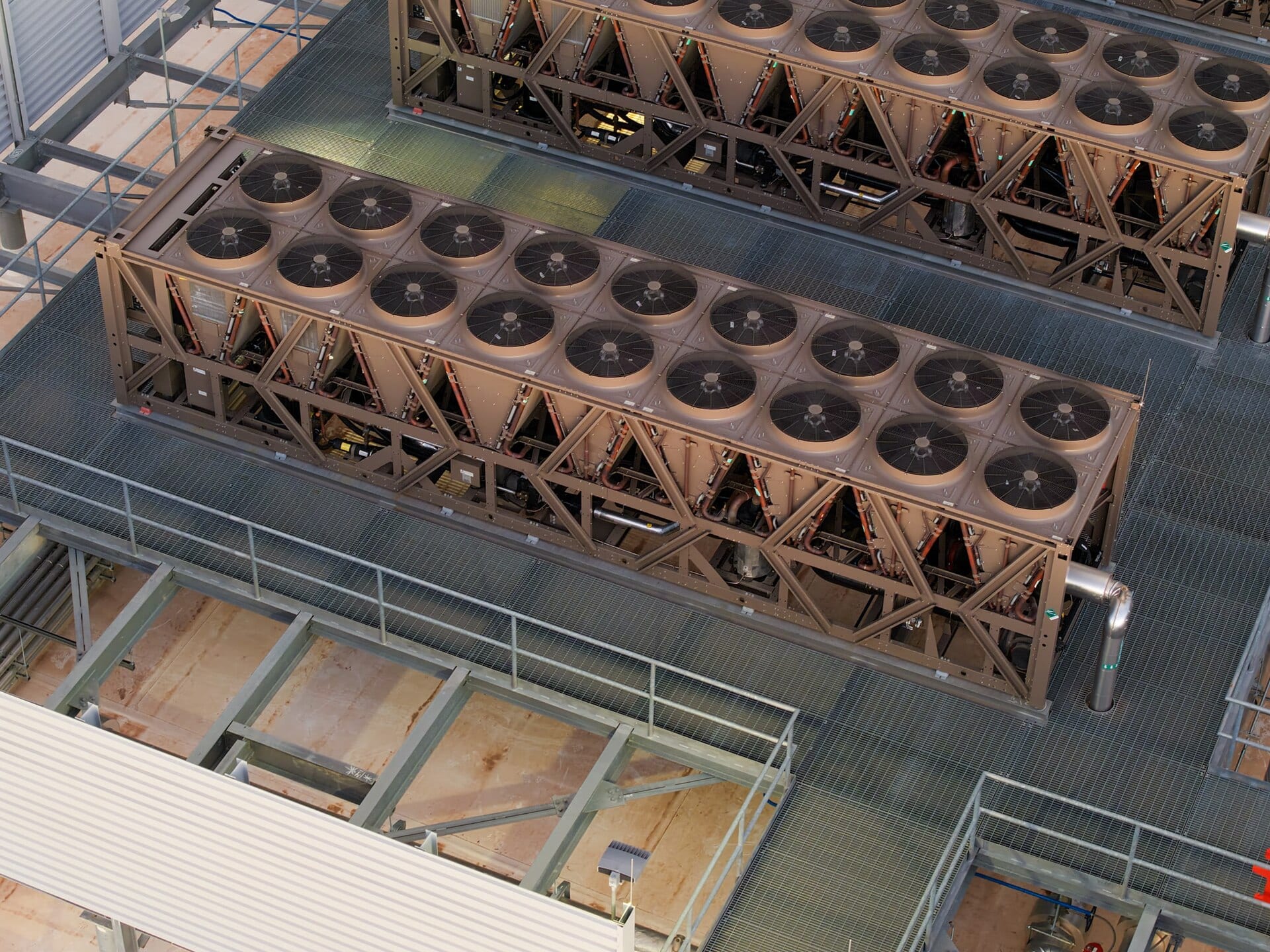 Rows of air-cooled chiller units with large fans on the roof of a data center, seen from above