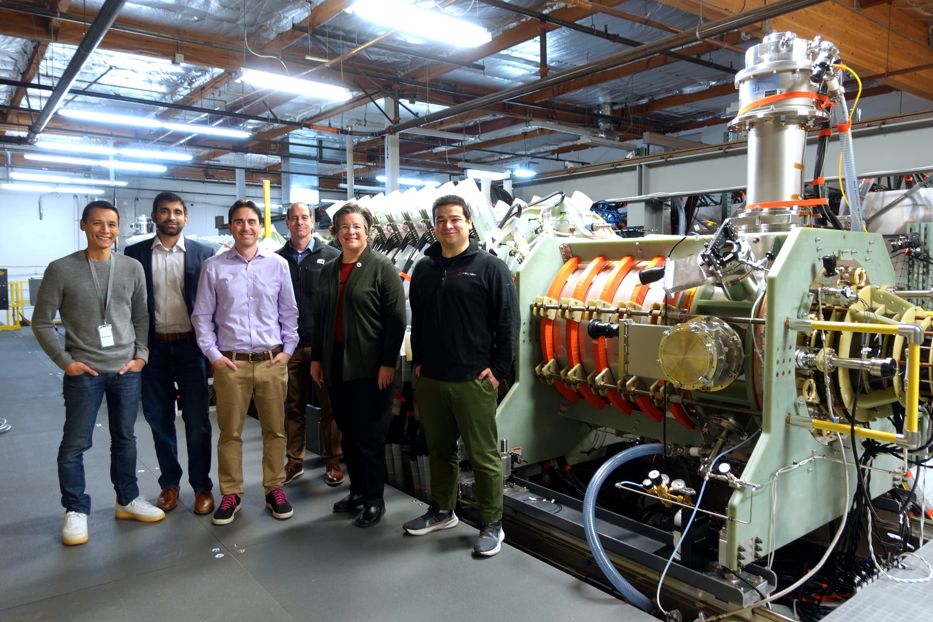 Visitors stand beside Helion's plasma injector machine, the fusion device line the company is scaling toward its Orion plant